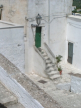 Weißes Haus , steile Stufen davor führen zu einer grünen Eingangstüre, Straßenlaterne an der Wand.